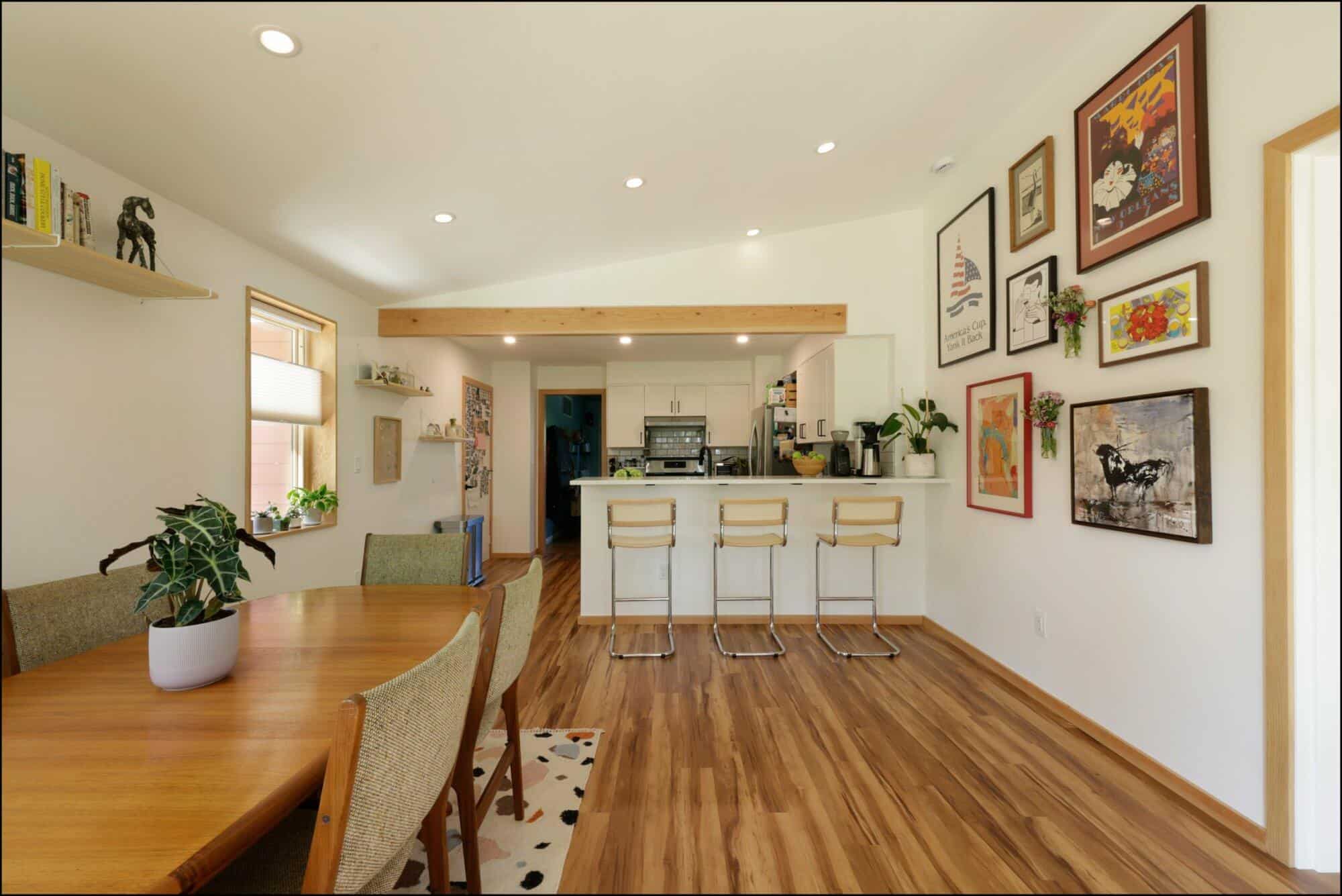 Dining room featuring a wooden table, stylish chairs, and a kitchen bar with stools; adorned with framed artwork and plants, showcasing modern interior design by ReCraft Home Remodeling in Portland.