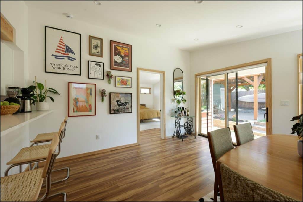 A well-lit dining area with a wooden table and four chairs. The room has a wall adorned with framed pictures, a sliding glass door, and a doorway leading to a bedroom. A well-lit dining area with a wooden table and four chairs. The room has a wall adorned with framed pictures, a sliding glass door, and a doorway leading to a bedroom.