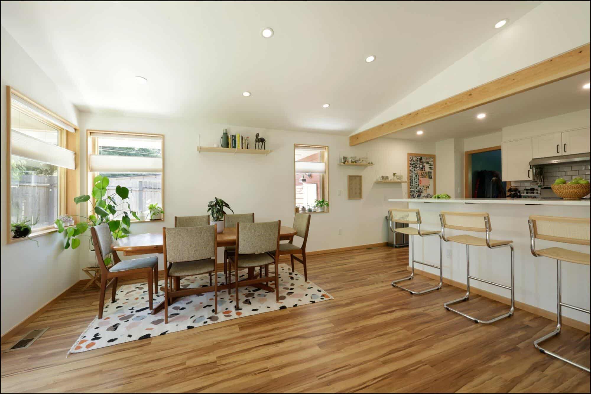 Modern dining area featuring a wooden dining table surrounded by chairs, an open kitchen with bar stools, and large windows allowing natural light, showcasing ReCraft Home Remodeling's interior design expertise in Portland.