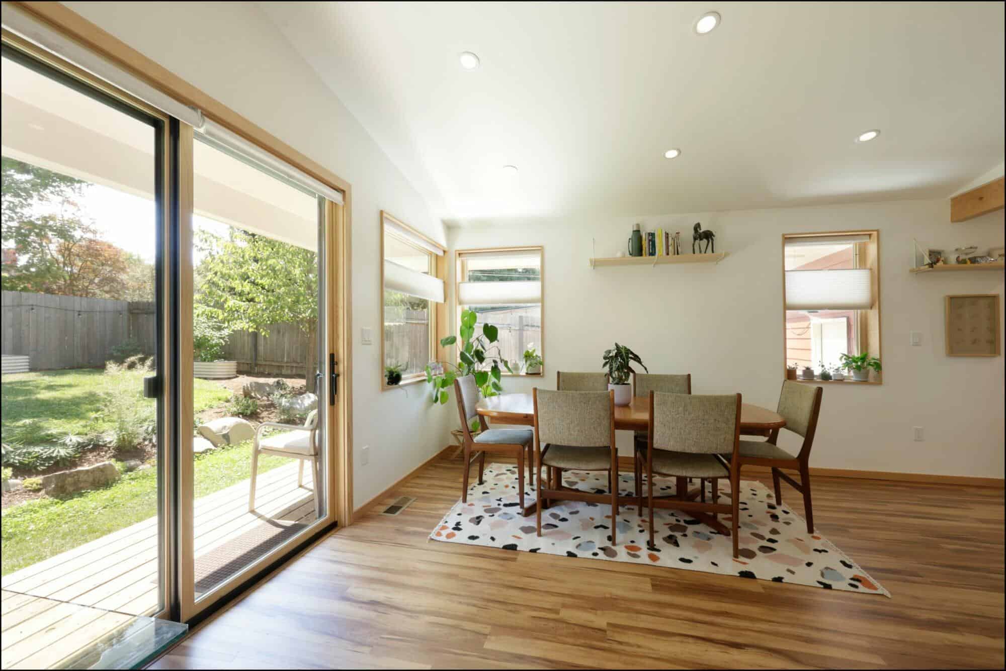 Modern dining room with wooden table and chairs, large windows showcasing garden view, natural light illuminating the space, designed by ReCraft Home Remodeling in Portland.