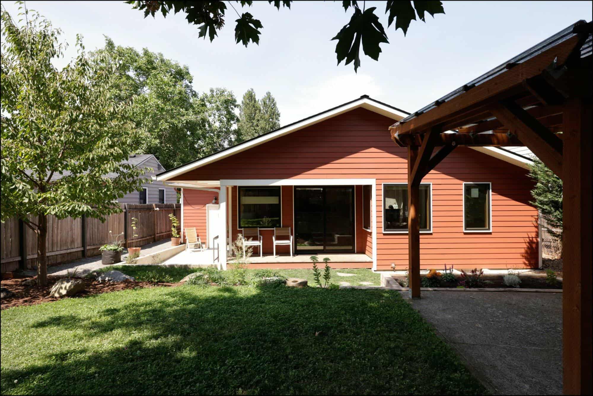 Exterior view of a remodeled home with a red facade, large windows, and a spacious back porch, showcasing landscaping and outdoor living space in a Portland residential setting.