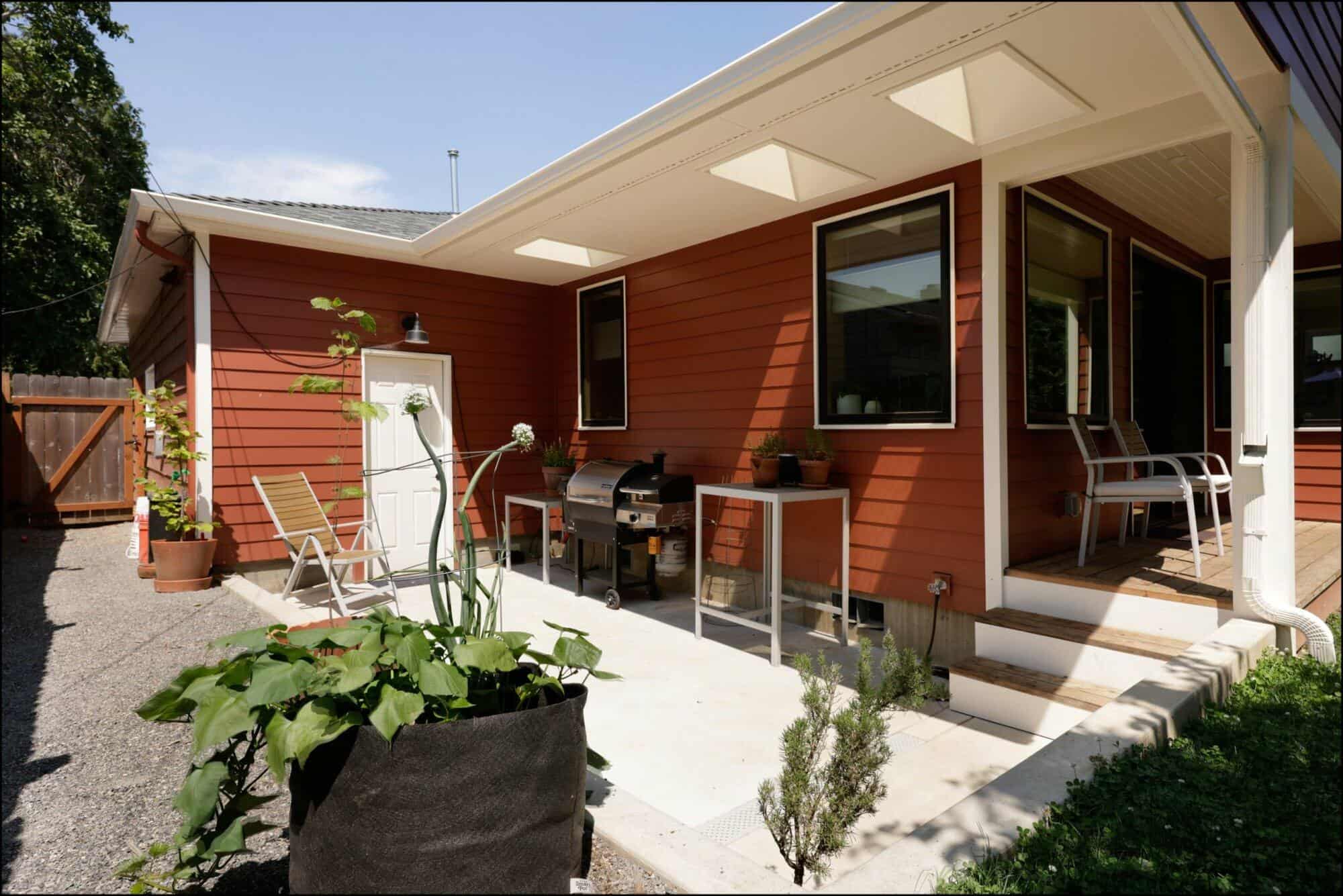 Exterior view of a remodeled patio featuring a red house, outdoor seating, and potted plants, showcasing ReCraft Home Remodeling's design work in Portland.