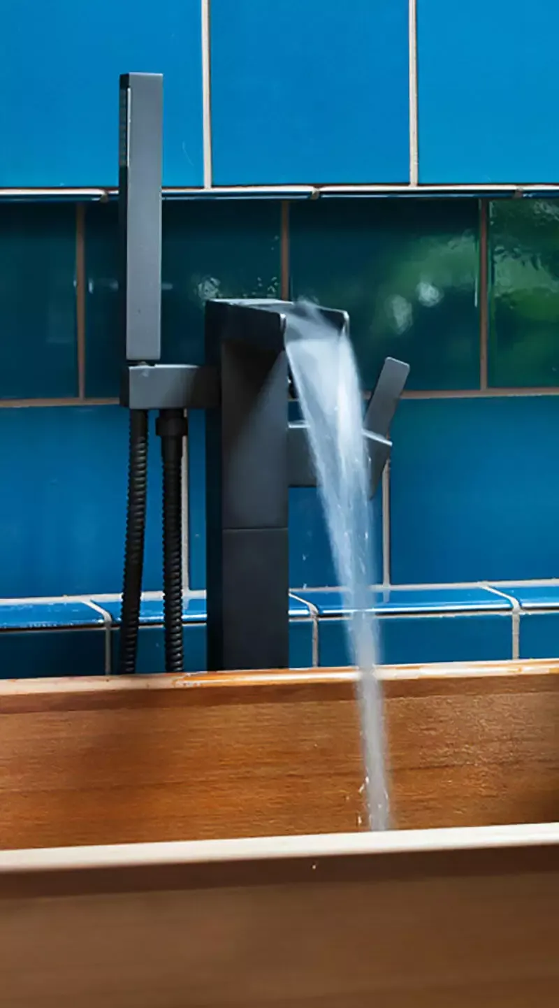 Water flows from a modern black faucet into a wooden sink against a blue tiled background.