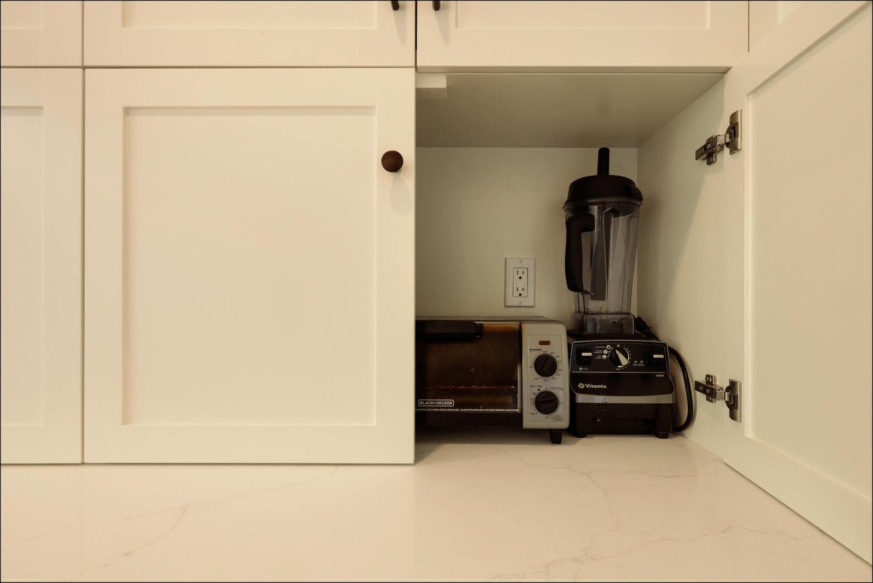 Open kitchen cabinet showing a toaster oven and a black blender on a white countertop. Open kitchen cabinet showing a toaster oven and a black blender on a white countertop.