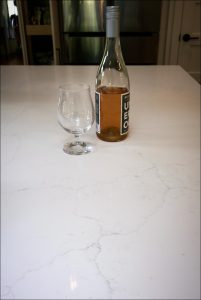 A bottle of rosé wine and an empty glass on a marble countertop.