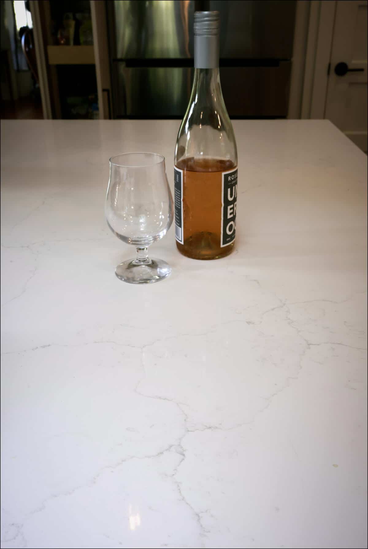 A bottle of rosé wine and an empty glass on a marble countertop. A bottle of rosé wine and an empty glass on a marble countertop.