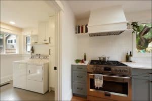 Modern kitchen with stainless steel stove next to a laundry area featuring a washer and dryer. White cabinets and light-colored walls create a bright atmosphere.
