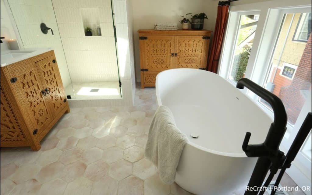 Modern bathroom by a NARI Remodeler of the Year, featuring a white freestanding tub, glass-enclosed shower, carved wooden cabinets, and natural light from large windows—a stunning residential addition.