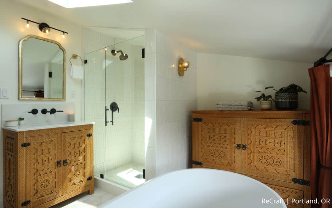 A bathroom with carved wooden cabinets, a glass shower, white walls, a round bathtub, and potted plants on the cabinet showcases a stunning before and after transformation from this nari residential addition.