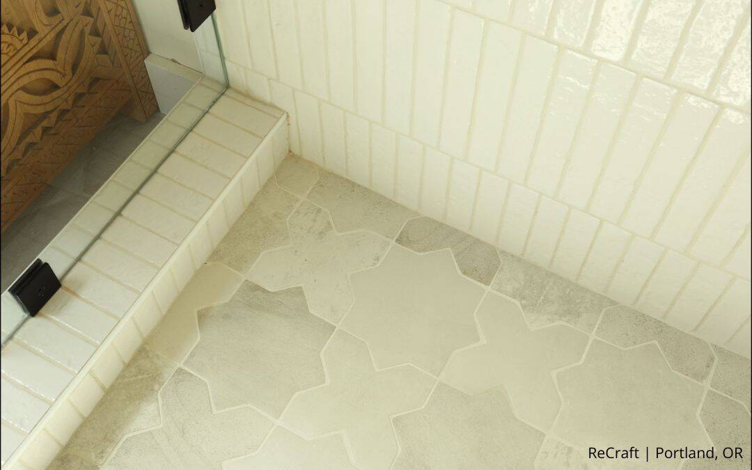 Close-up of a bathroom corner showcases geometric-patterned floor tiles, glossy wall tiles, and a glass shower enclosure—a stunning transformation by our remodeler of the year.