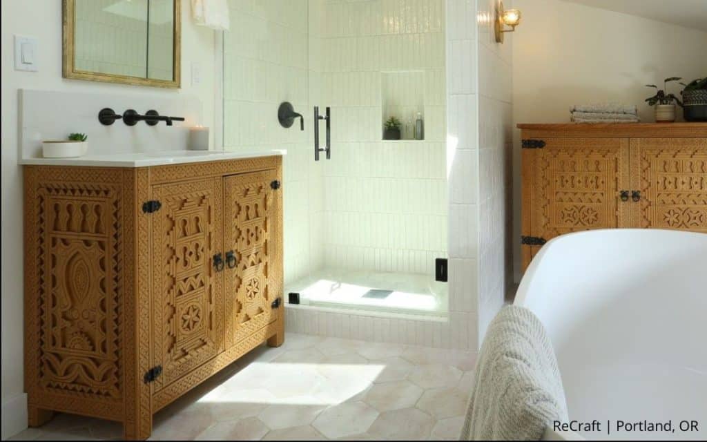 Experience this award-winning remodel: a bathroom featuring carved wooden cabinets, a glass shower with white tile, a white bathtub, and hexagonal floor tiles—a true before and after transformation by Remodeler of the Year.