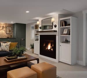 A cozy living room with a lit fireplace, white built-in shelves, a mirror above the mantel, a wooden coffee table, and neutral-colored seating.
