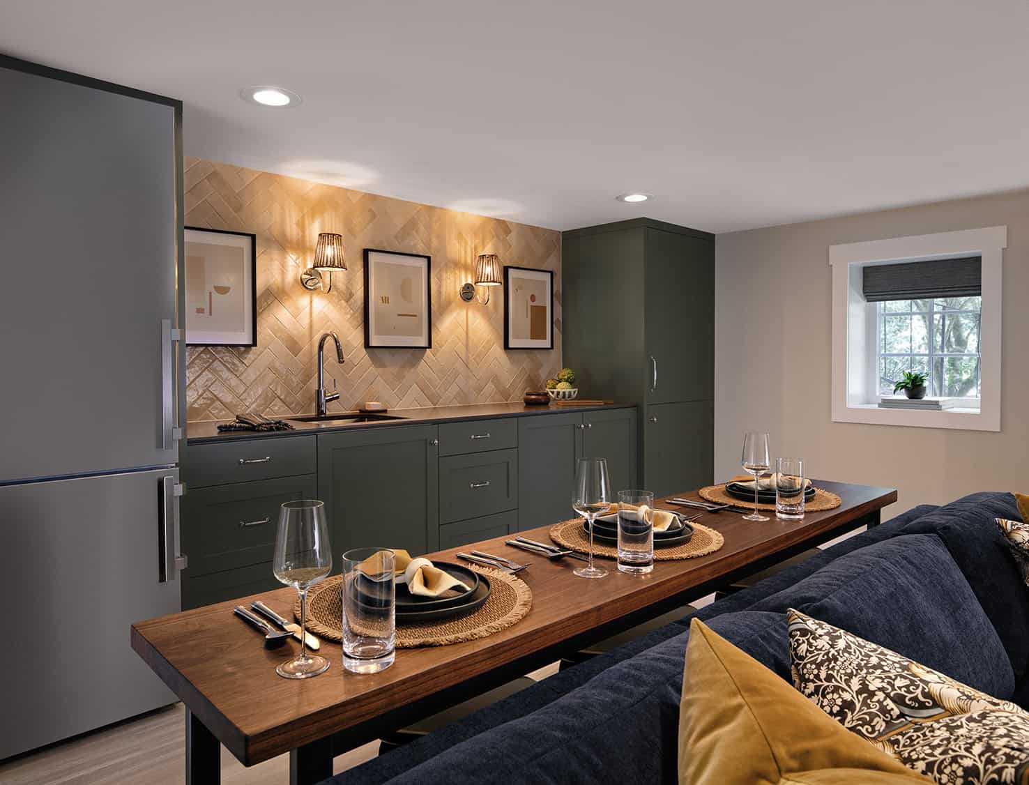 Modern basement kitchen and dining area featuring green cabinetry, wood dining table set for four, stylish decor, and natural light from nearby window, showcasing ReCraft Home Remodeling's expertise in basement transformations.