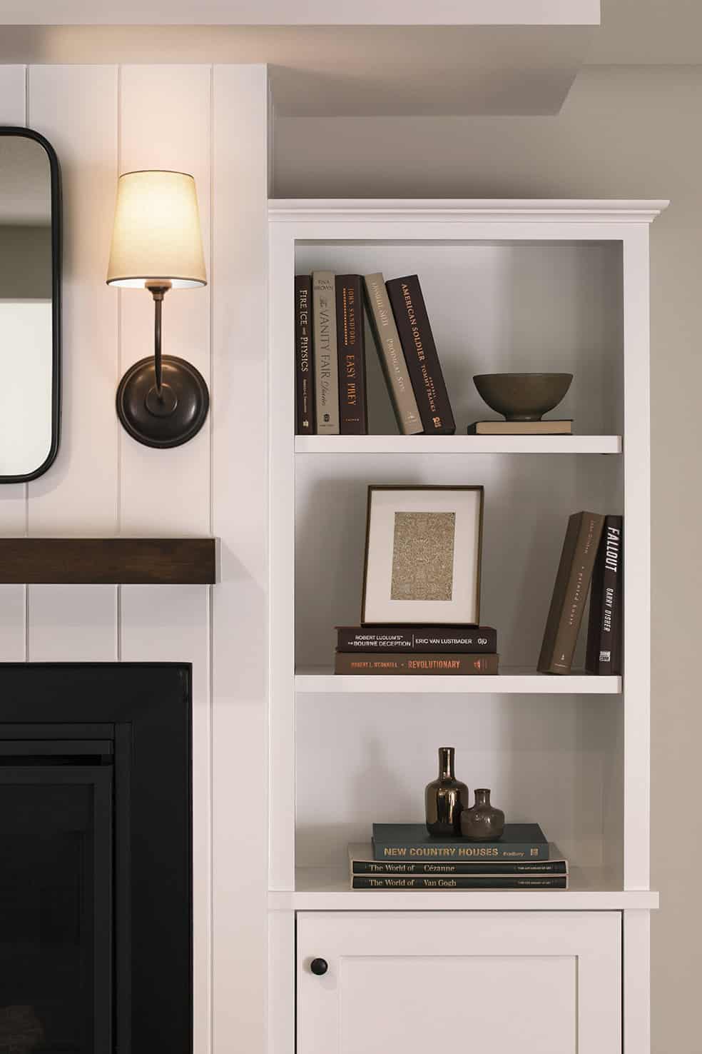 Modern white bookshelf with decorative items, books, and a wall-mounted sconce, showcasing stylish basement remodeling by ReCraft Home Remodeling Portland.