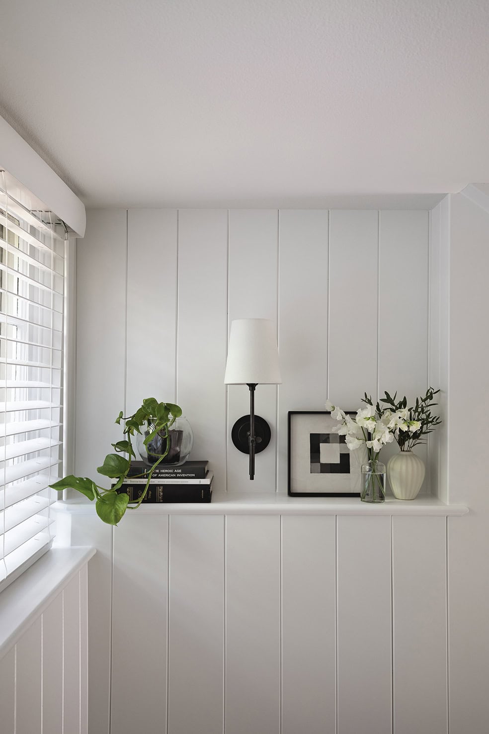 Cozy basement corner featuring a wall-mounted lamp, potted plant, decorative books, and a vase of flowers, showcasing ReCraft Home Remodeling's design aesthetics in basement renovations.