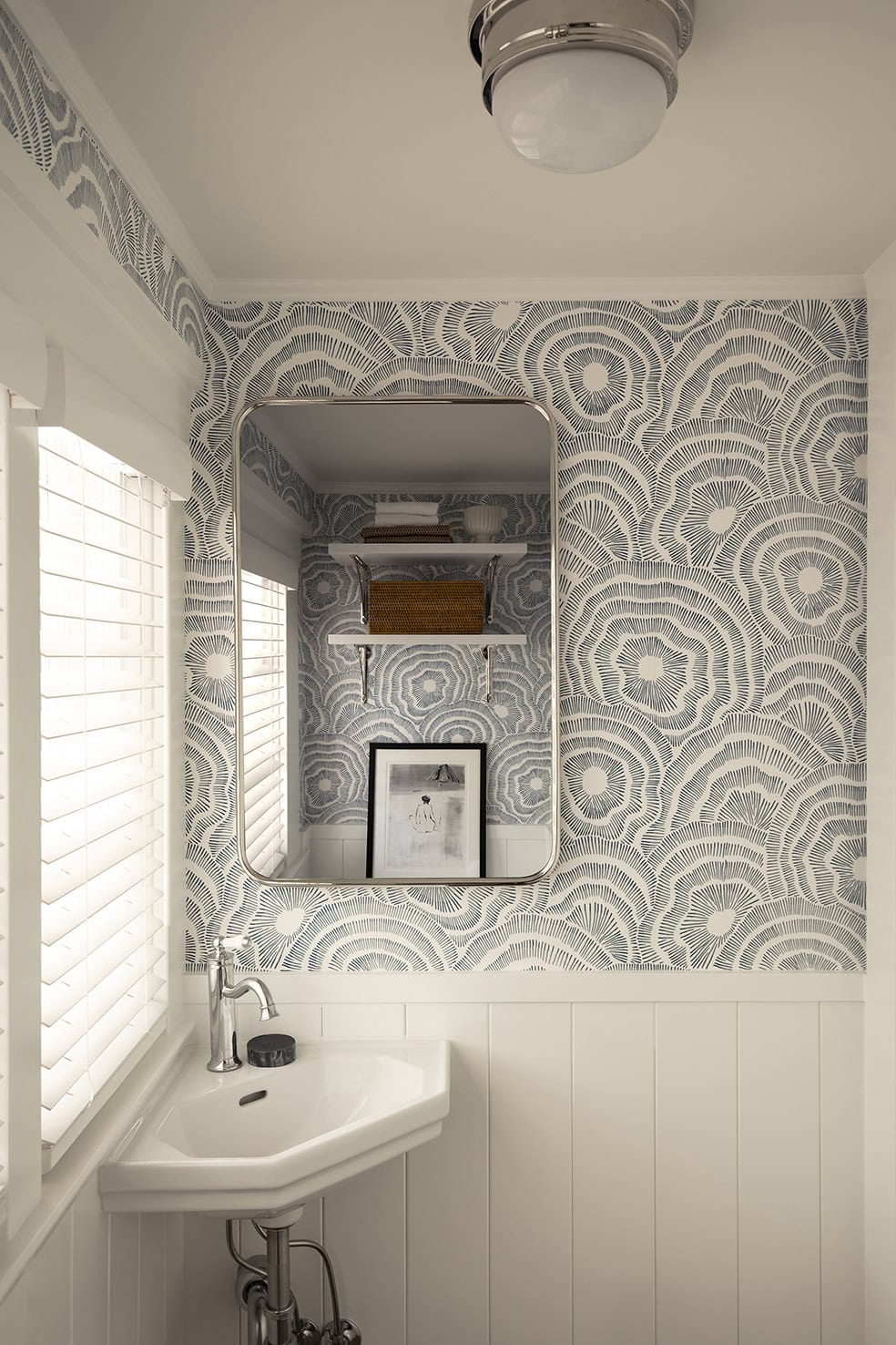Modern bathroom with decorative patterned wallpaper, corner sink, and natural light from window, showcasing ReCraft Home Remodeling's design expertise in basement renovations.