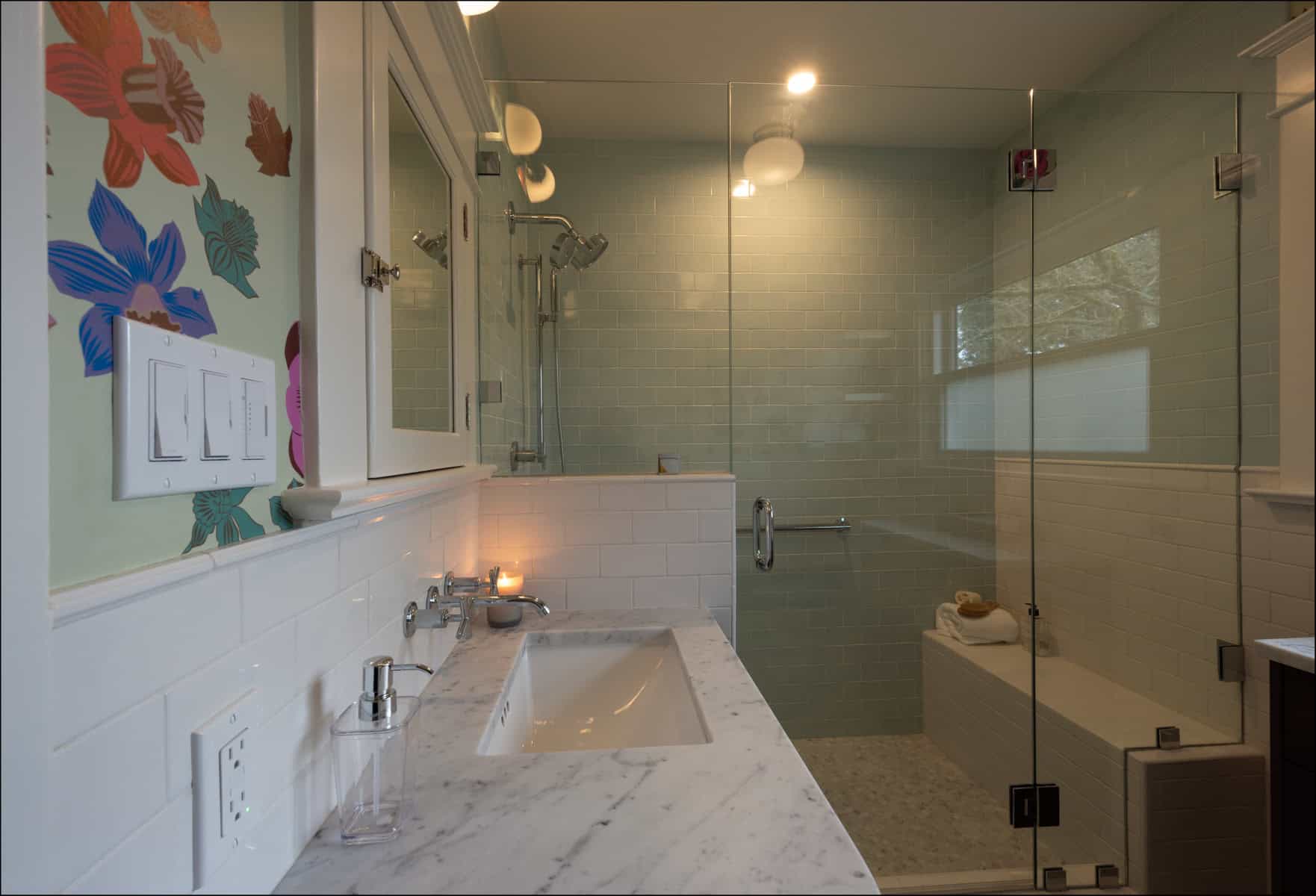 A modern bathroom with a marble countertop, a rectangular sink, wall-mounted fixtures, and a glass-enclosed shower with light green tiles and a bench.