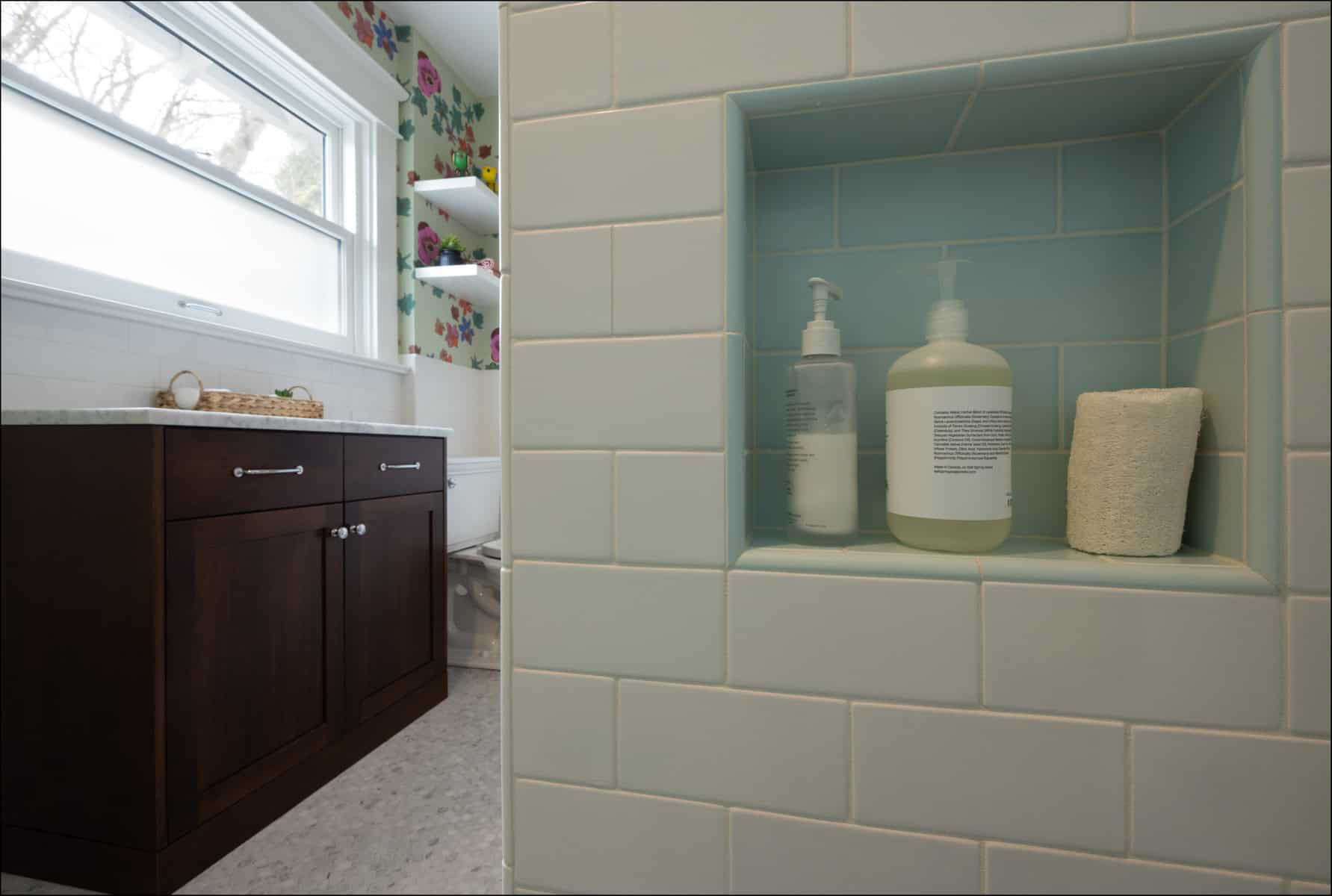 A tiled shower niche with two pump bottles and a rolled towel is shown in the foreground; a bathroom vanity and window are visible in the background.