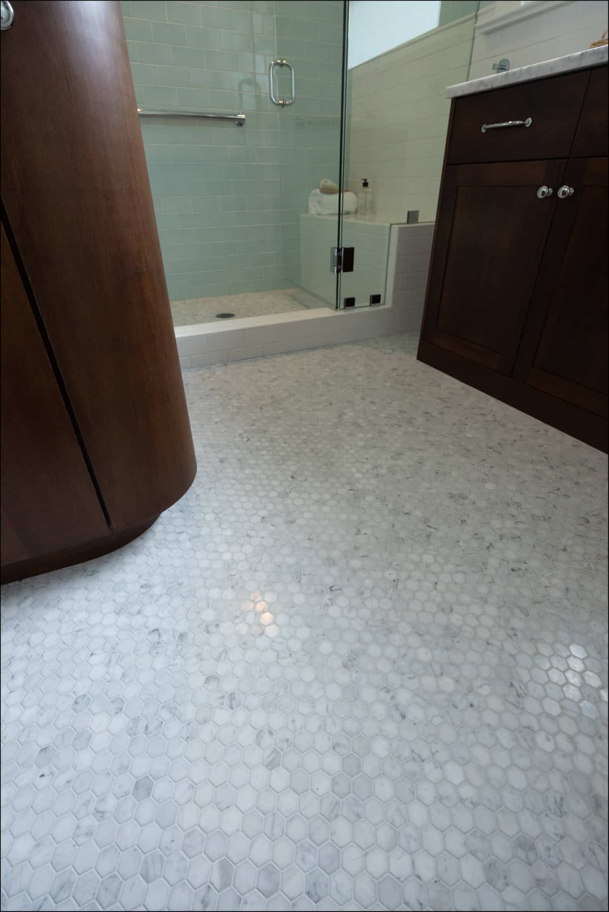 Bathroom with hexagonal marble tile flooring, dark wood vanity cabinets, and a glass-enclosed shower with light blue subway tile walls.