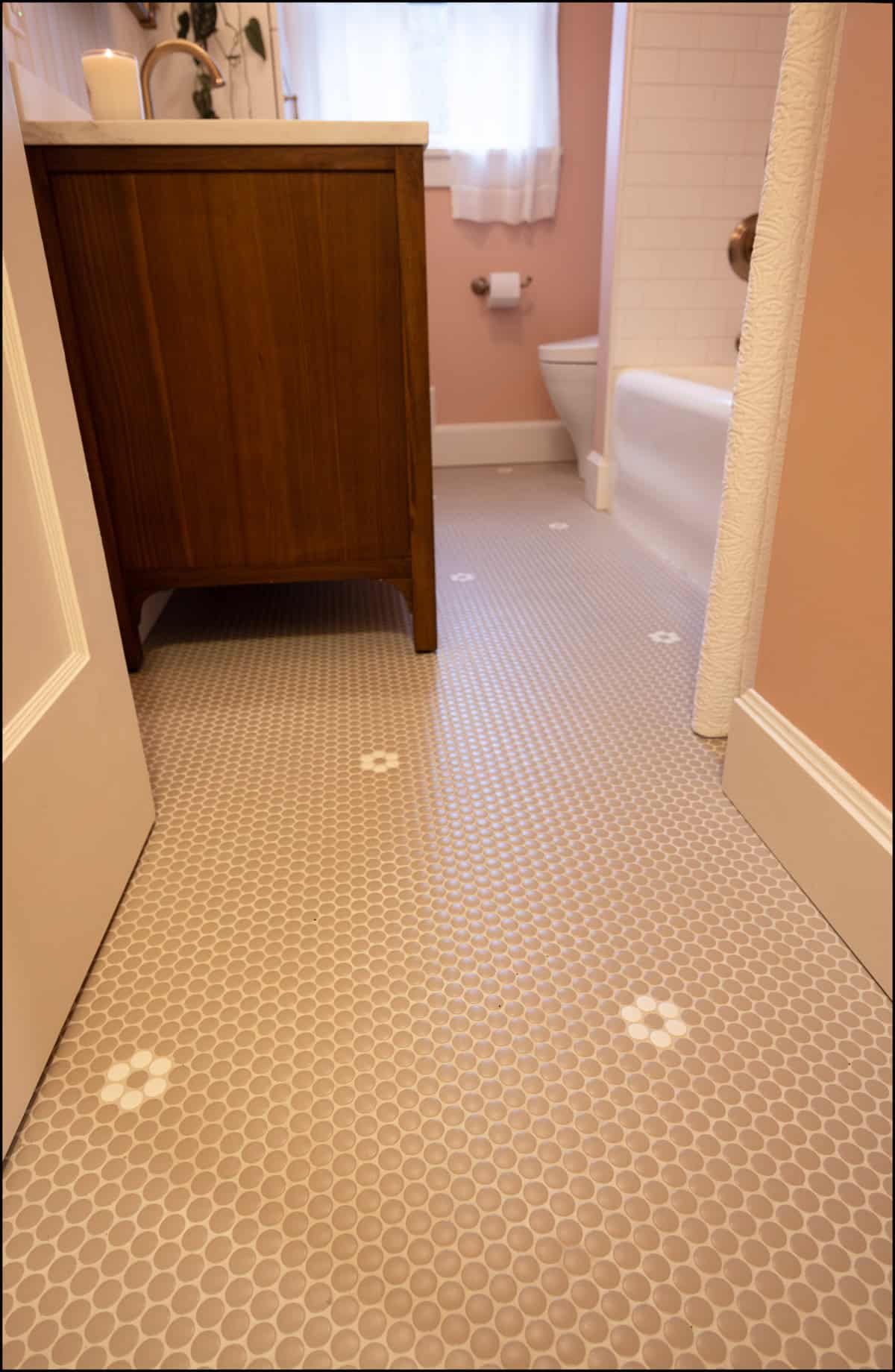 Bathroom with pink walls, a vanity with a wood cabinet, a toilet, bathtub, and gray hexagonal tile floor with white flower patterns.