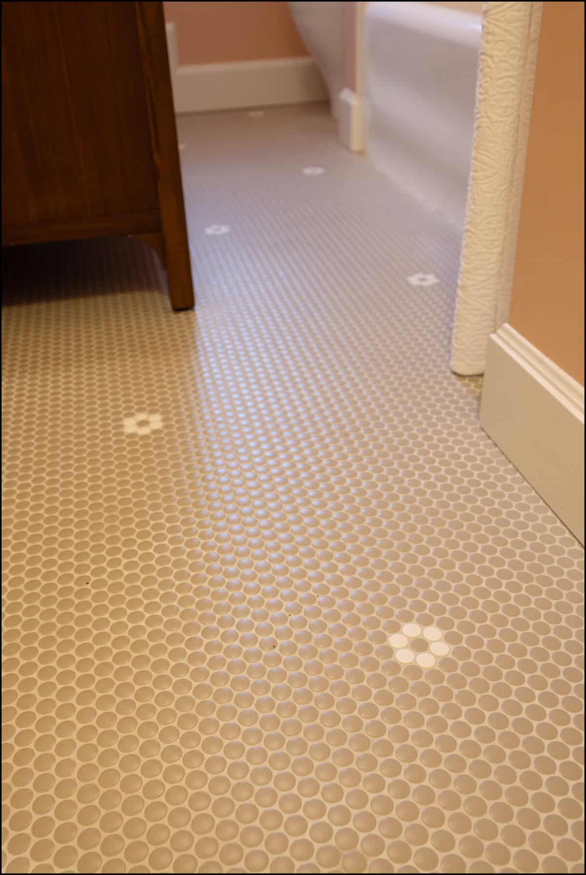 Bathroom floor with small beige hexagonal tiles and occasional white hexagon flower patterns, next to a bathtub, wooden cabinet, and baseboard.