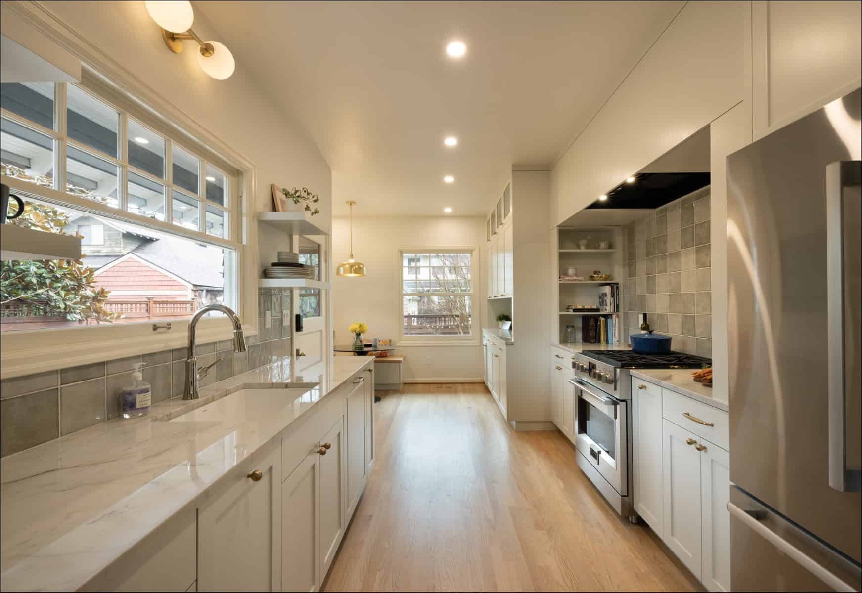 Modern kitchen with white cabinets, marble countertops, stainless steel appliances, wooden floor, and large window overlooking a side yard. Modern kitchen with white cabinets, marble countertops, stainless steel appliances, wooden floor, and large window overlooking a side yard.