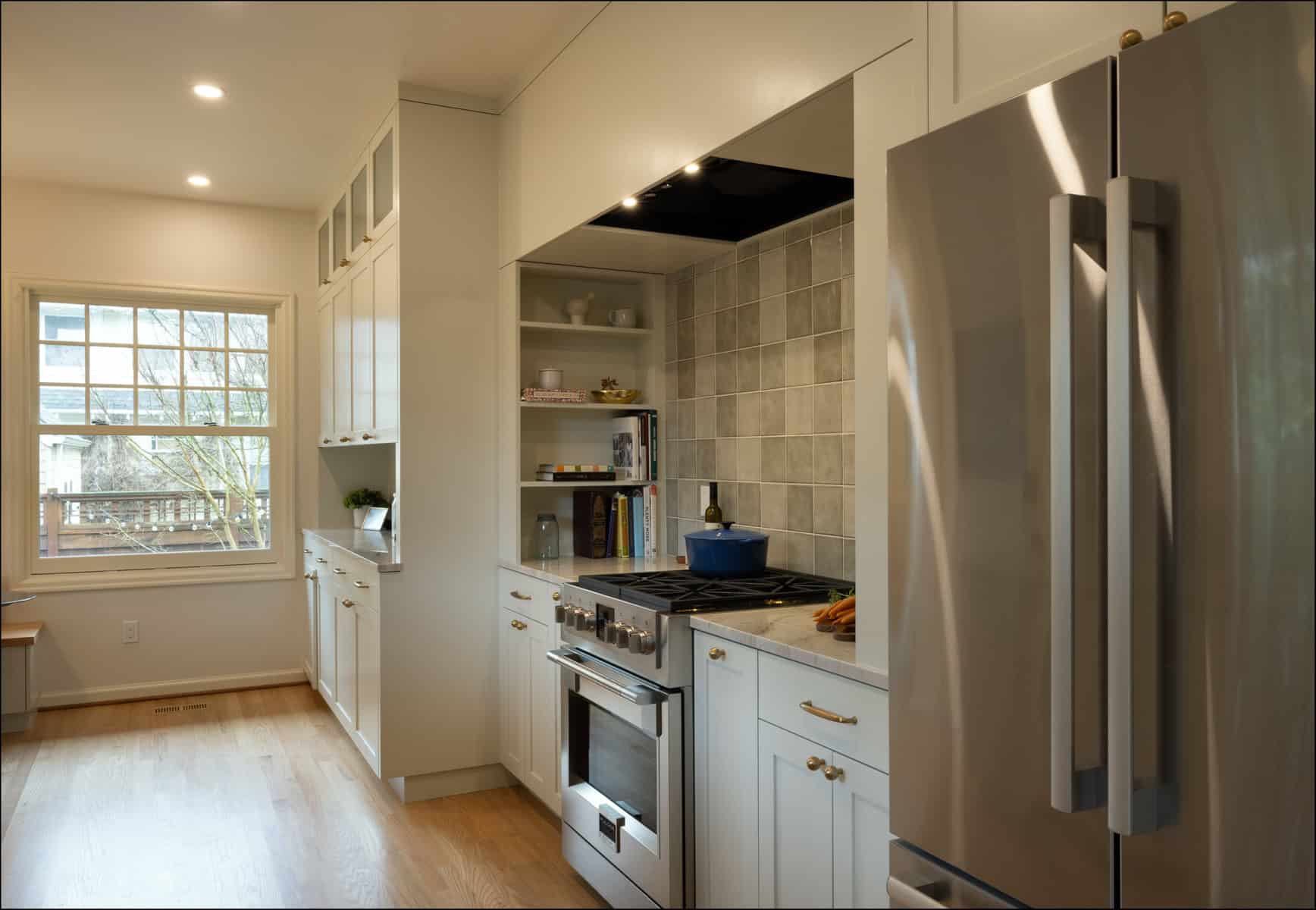 Modern kitchen with stainless steel refrigerator, gas stove, oven, white cabinets, tiled backsplash, wooden floor, and a window letting in natural light. Modern kitchen with stainless steel refrigerator, gas stove, oven, white cabinets, tiled backsplash, wooden floor, and a window letting in natural light.