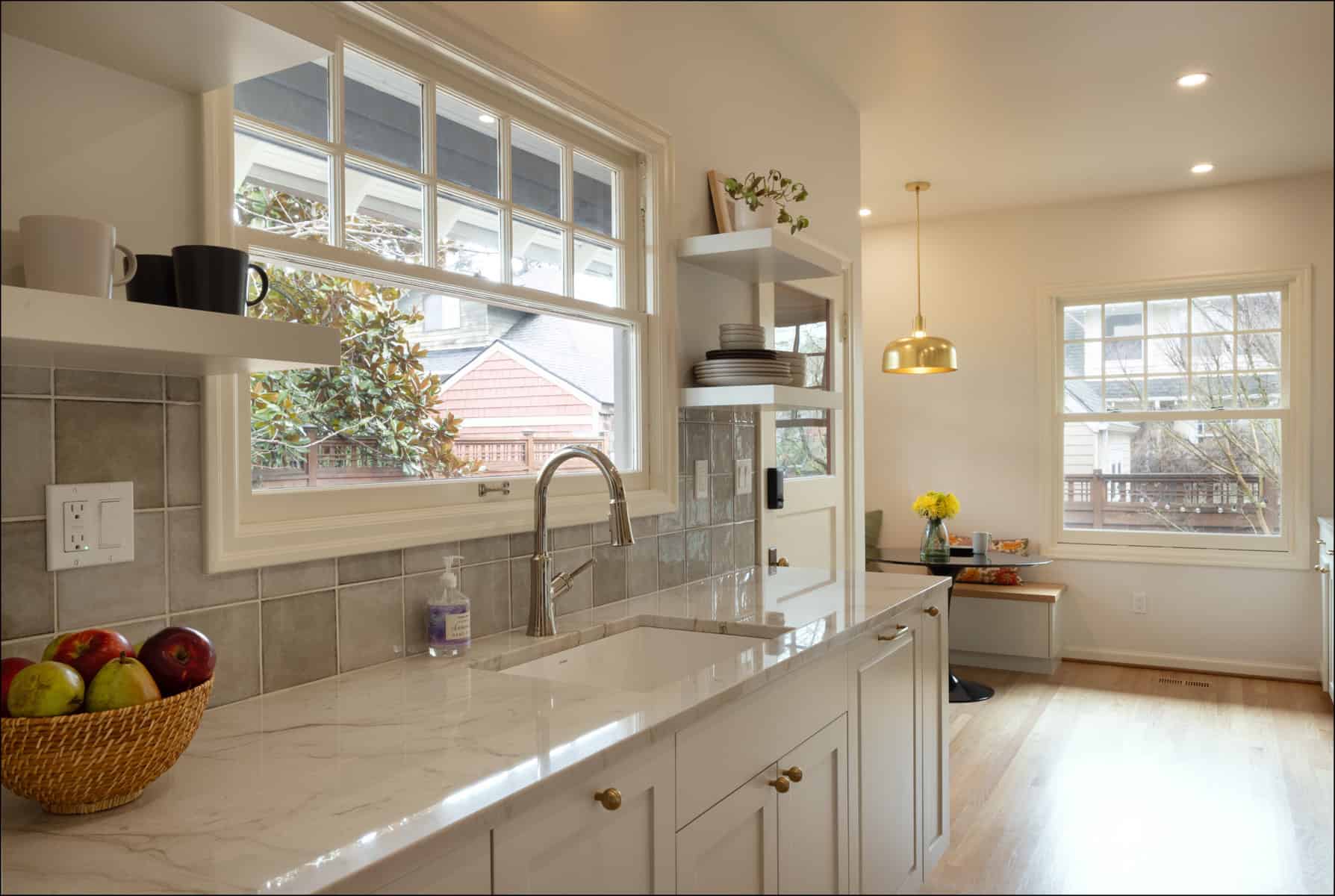 Bright kitchen with marble countertop, white cabinets, a sink with a modern faucet, a basket of apples, open shelves, and large windows letting in ample natural light. Bright kitchen with marble countertop, white cabinets, a sink with a modern faucet, a basket of apples, open shelves, and large windows letting in ample natural light.