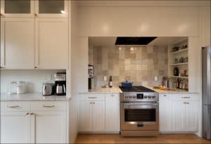 Modern kitchen with white cabinets, stainless steel stove, marble countertops, open shelves with kitchen items, and jars of sugar and flour on the left counter.