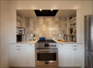 Modern kitchen with a stainless steel stove and oven, white cabinets, tiled backsplash, open shelves, and vegetables and a knife on the countertop.