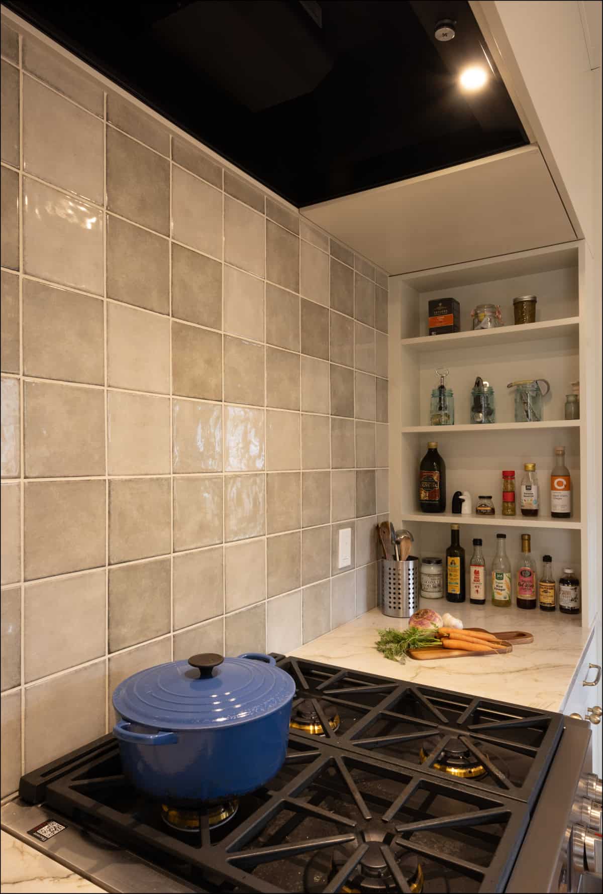 A blue Dutch oven sits on a gas stove in a kitchen with gray tiled backsplash; shelves hold bottles, jars, and kitchen tools. A blue Dutch oven sits on a gas stove in a kitchen with gray tiled backsplash; shelves hold bottles, jars, and kitchen tools.
