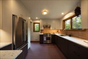 Modern kitchen with stainless steel appliances, white upper cabinets, dark lower cabinets, light countertops, and large windows letting in natural light.