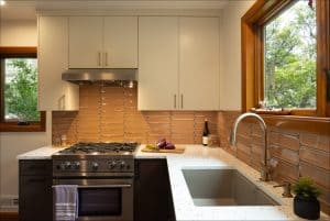 Modern kitchen with a gas stove, beige tile backsplash, white cabinets, a countertop with vegetables, and a large sink next to a window with a wooden frame.