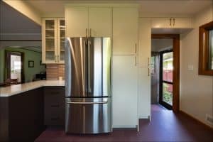 A modern kitchen features a stainless steel French door refrigerator, white cabinets, a countertop, and a door leading outside.