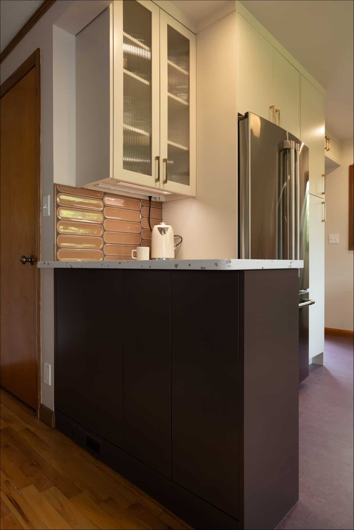 Modern kitchen corner with dark lower cabinets, white upper cabinets with glass doors, a marble countertop, a stainless steel fridge, and a pink tile backsplash. Modern kitchen corner with dark lower cabinets, white upper cabinets with glass doors, a marble countertop, a stainless steel fridge, and a pink tile backsplash.