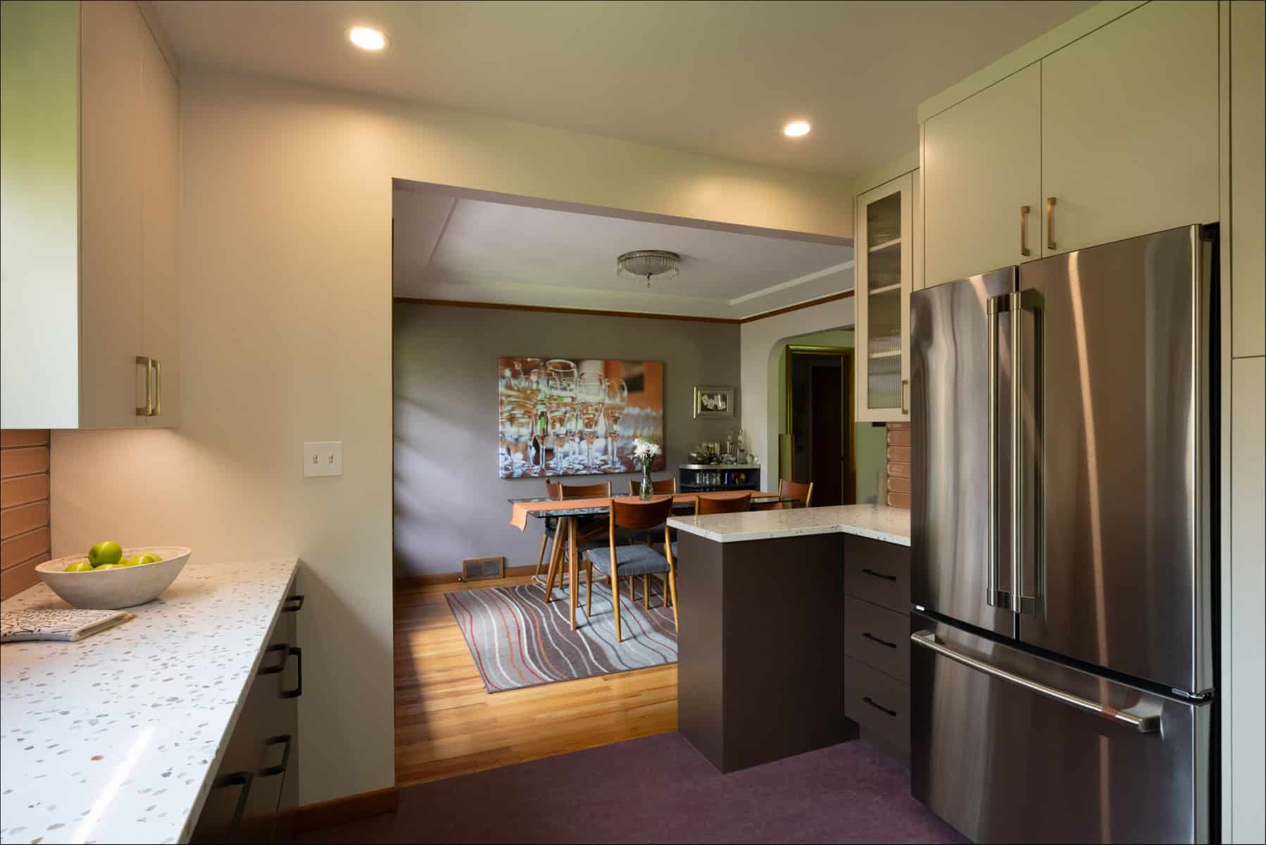 Modern kitchen with stainless steel refrigerator and white cabinets, leading into a dining area with a wooden table and chairs on a striped rug. Modern kitchen with stainless steel refrigerator and white cabinets, leading into a dining area with a wooden table and chairs on a striped rug.