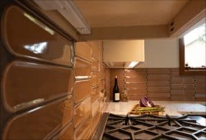 Close-up of a kitchen with brown tile backsplash, a stove, a wine bottle, corks, and vegetables including asparagus and purple cabbage on a cutting board.
