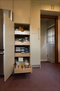 A kitchen pantry cabinet with four pull-out shelves containing assorted food items and containers is open, revealing organized storage.