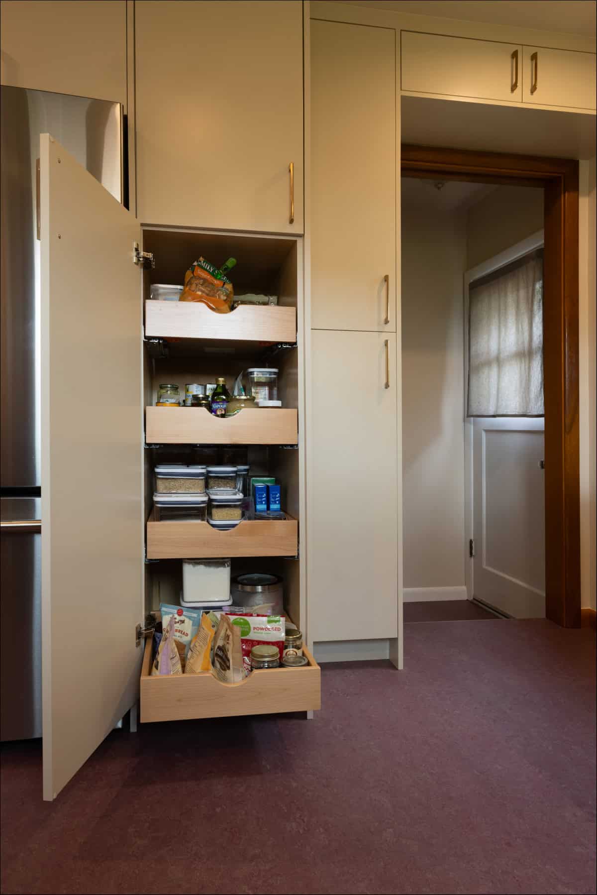 A kitchen pantry cabinet with four pull-out shelves containing assorted food items and containers is open, revealing organized storage. A kitchen pantry cabinet with four pull-out shelves containing assorted food items and containers is open, revealing organized storage.