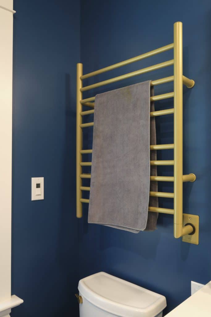 A gold towel warmer with a gray towel is mounted on a blue wall above a white toilet—one of the standout luxury bathroom features in this Portland home.