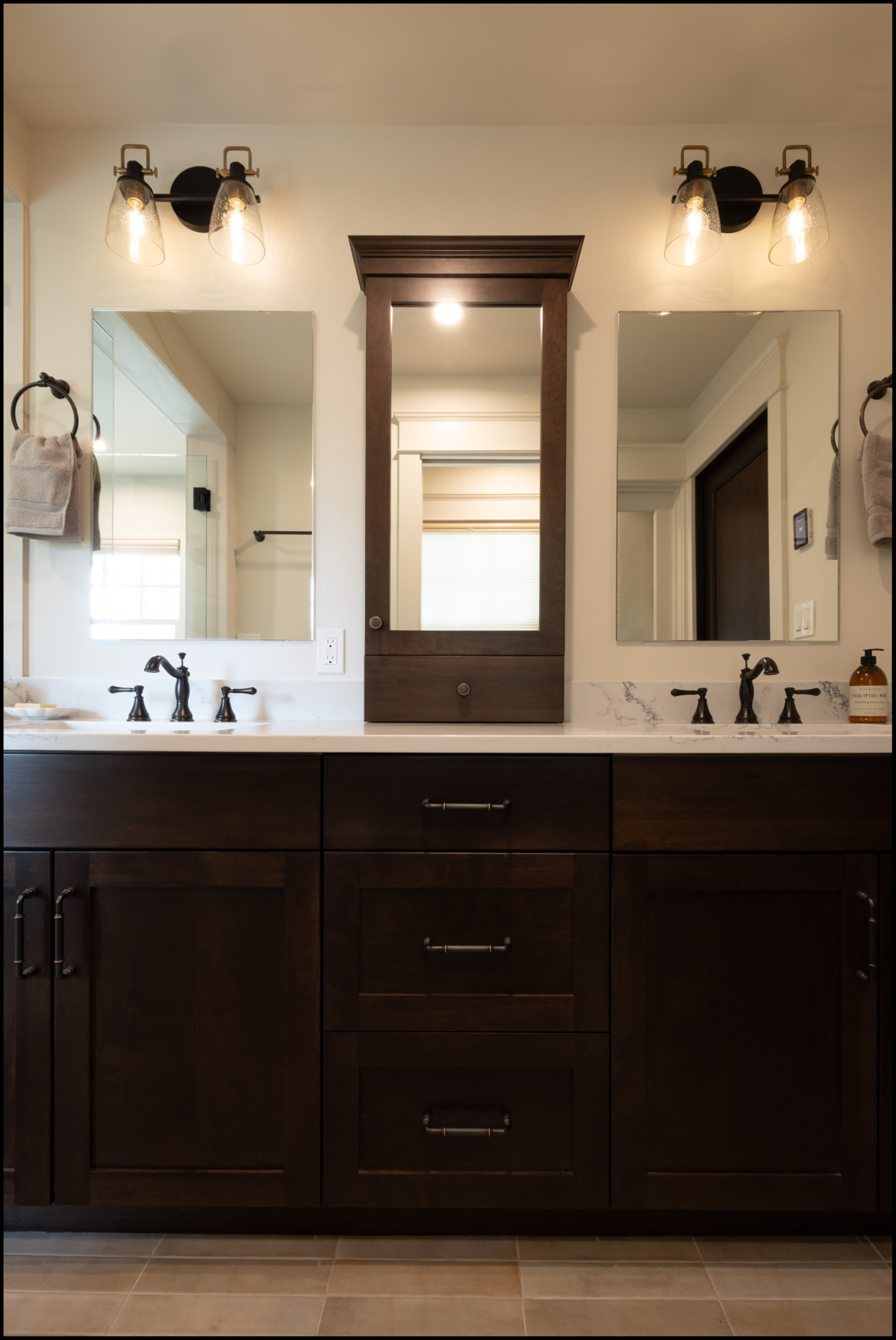 Double sink bathroom vanity with dark wood cabinets, two wall mirrors, a central medicine cabinet, and modern light fixtures above each mirror.