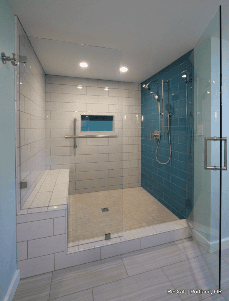 Modern walk-in shower with glass doors, white and blue tiled walls, built-in bench, grab bar, wall niche, handheld showerhead, and recessed ceiling lights—perfect for inspiring family basement ideas or your next basement remodel.