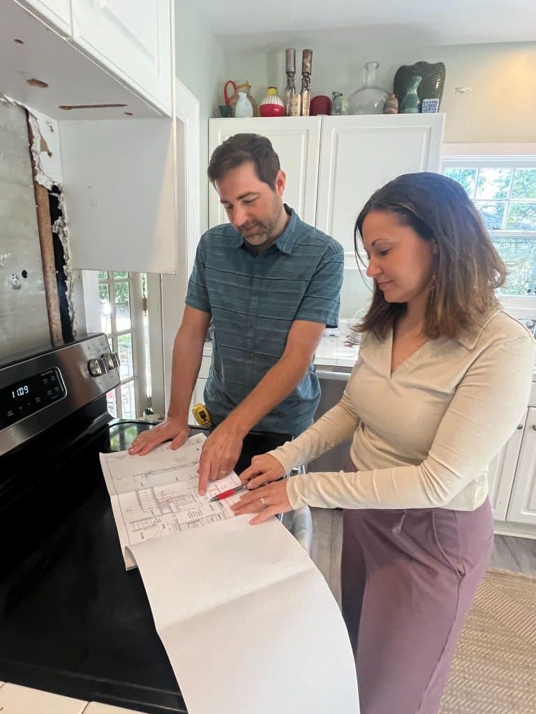 Top remodeling mistakes homeowners make - not having a clear plan. Two people stand in a kitchen looking over blueprints or plans laid out on a stove, discussing details together.