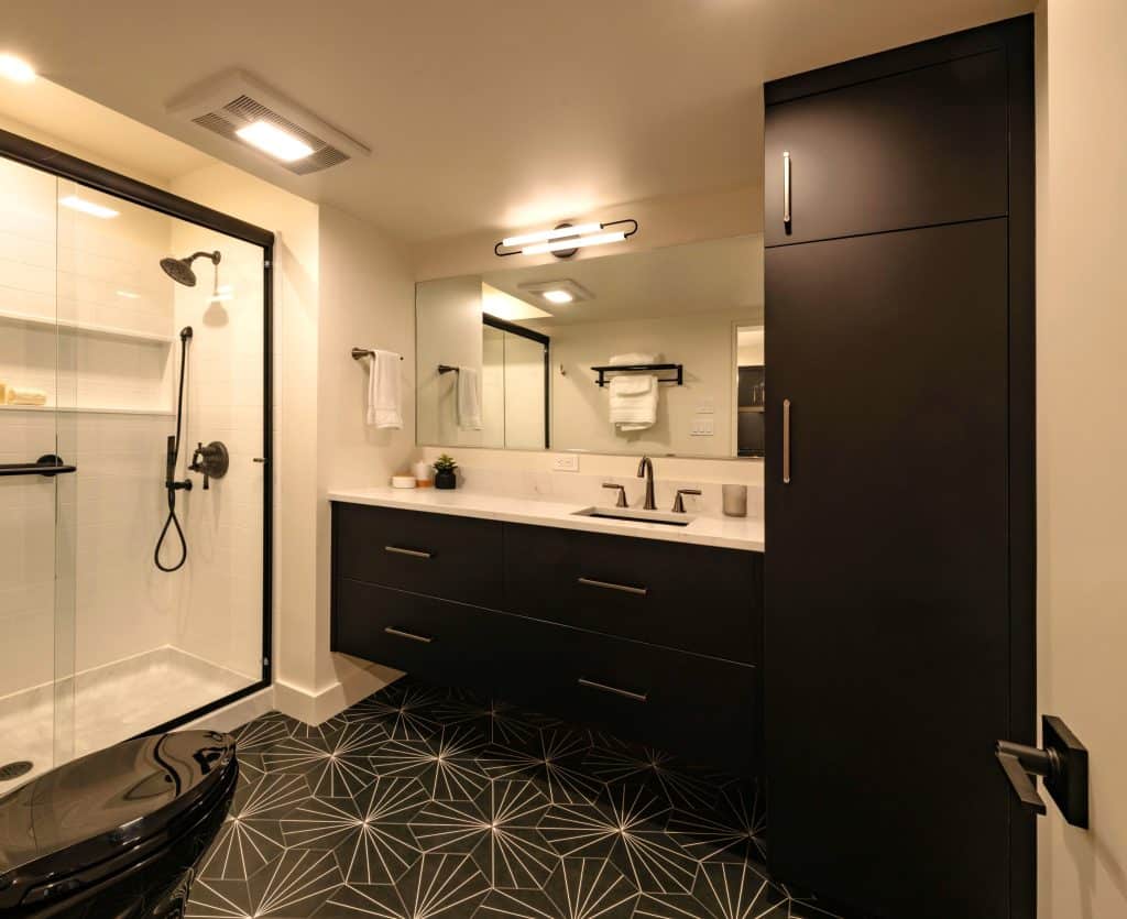 Modern bathroom design featuring a glass shower, sleek black cabinetry, and geometric tile flooring, showcasing ReCraft Home Remodeling's basement renovation expertise in Portland.