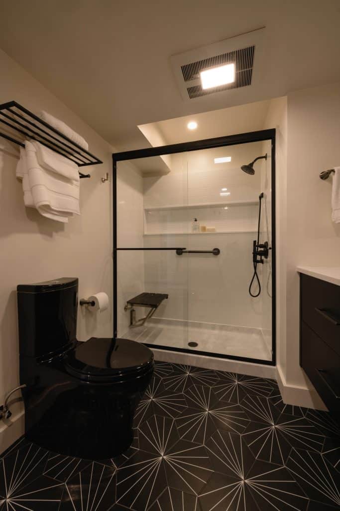 Modern bathroom design featuring a black toilet, glass shower enclosure, and geometric patterned floor tiles, showcasing ReCraft Home Remodeling's basement renovation expertise in Portland.