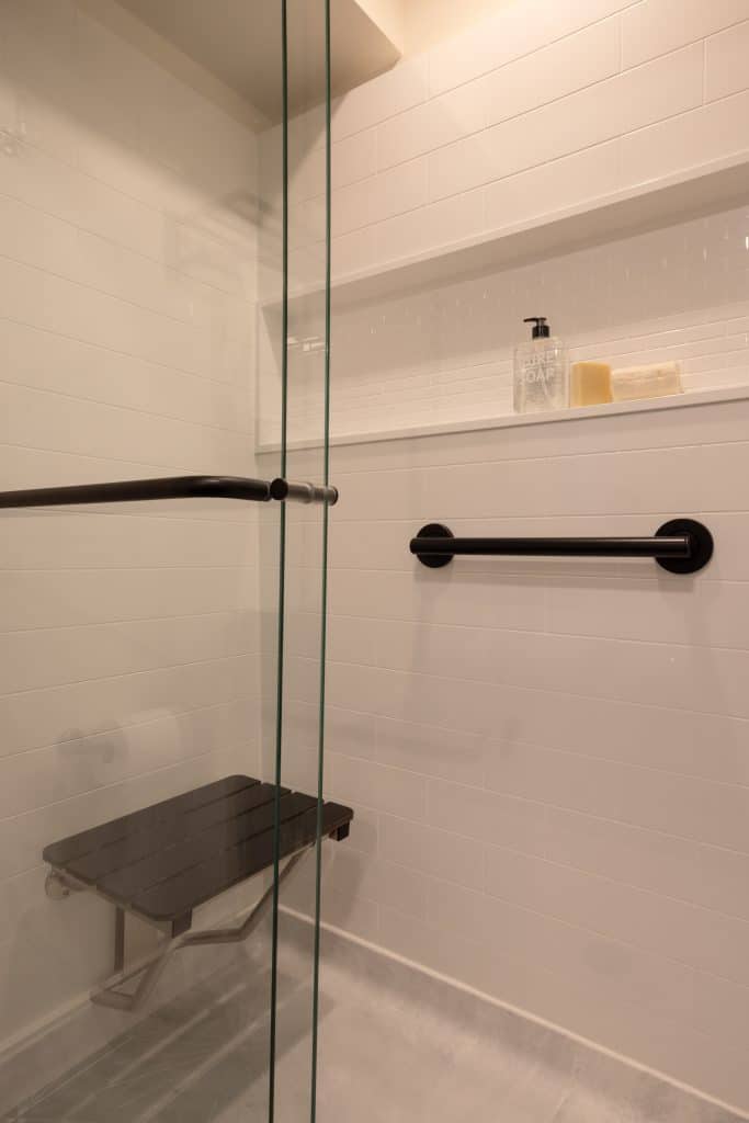 Modern glass shower enclosure with black fixtures, featuring a built-in bench and minimalist design, showcasing ReCraft Home Remodeling's basement renovation work in Portland.