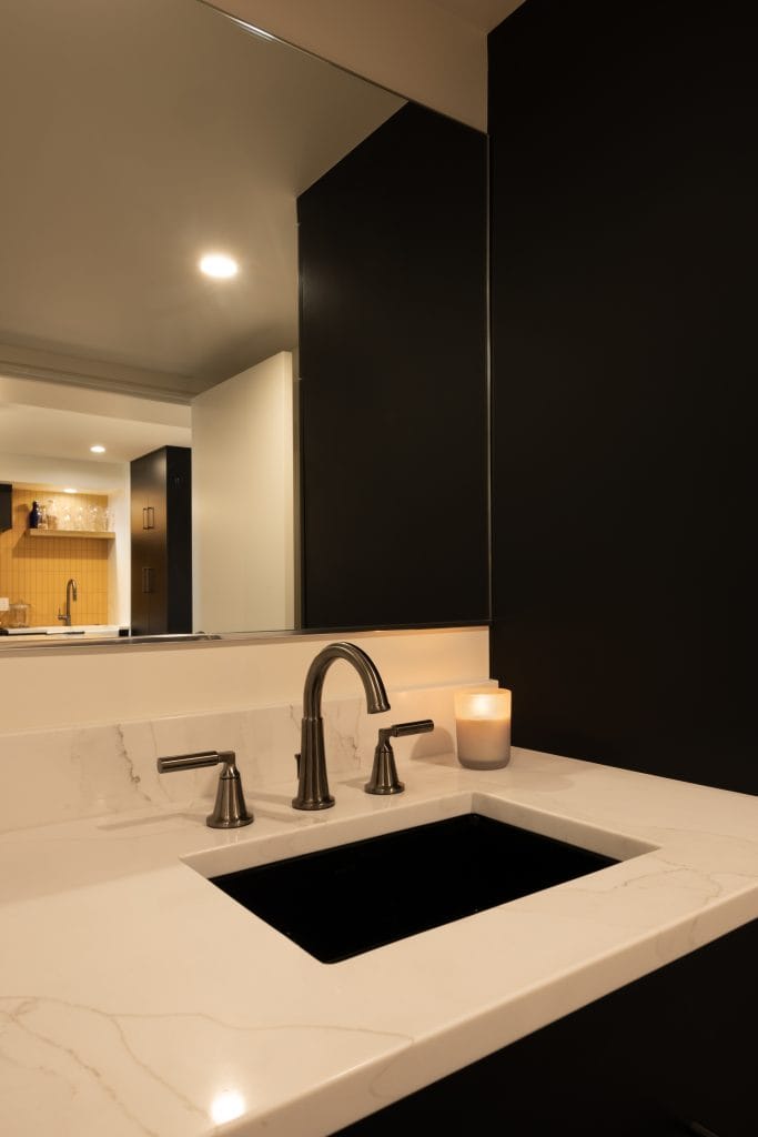 Modern bathroom sink with sleek black cabinetry, polished white countertop, and stylish faucets, showcasing a contemporary basement renovation by ReCraft Home Remodeling in Portland.