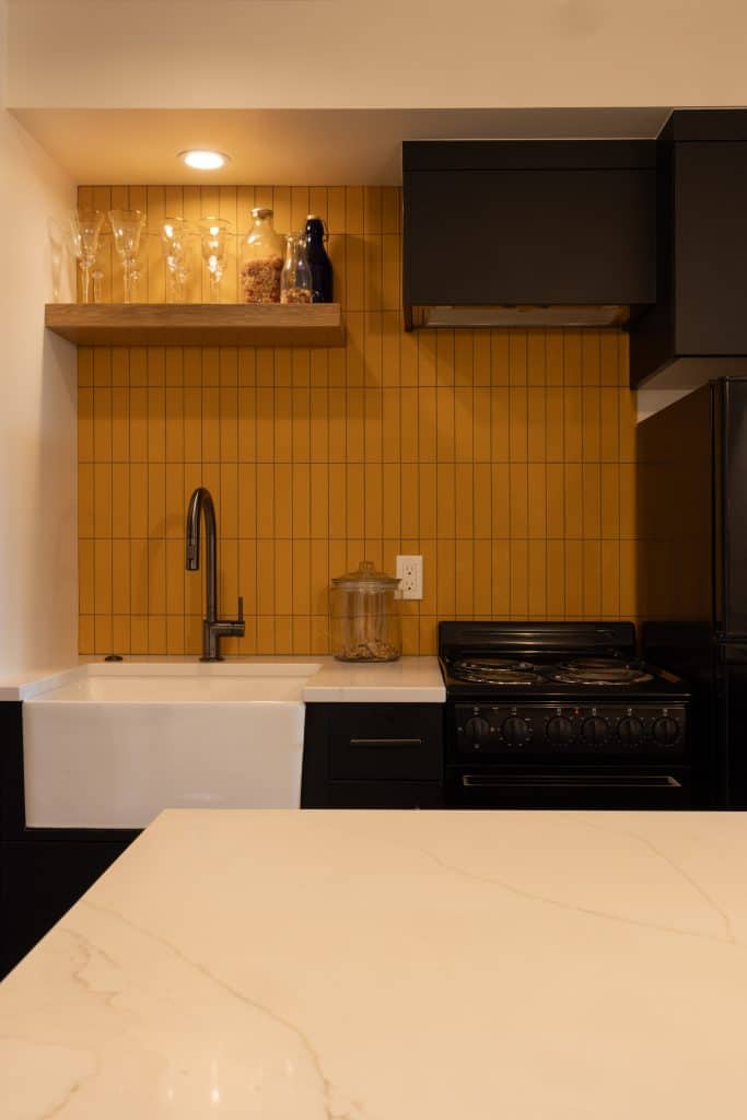 Modern basement kitchen renovation featuring a farmhouse sink, sleek black cabinetry, and a vibrant yellow tiled backsplash, showcasing ReCraft Home Remodeling's design expertise in Portland.