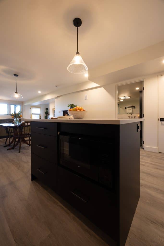 Modern kitchen island with dark cabinetry, integrated microwave, and pendant lighting, showcasing a stylish basement remodeling project by ReCraft Home Remodeling in Portland.