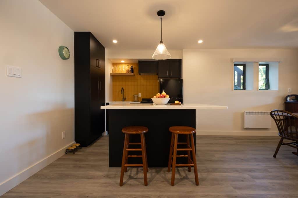 Modern basement kitchen with black cabinetry, white countertop, and two wooden stools, showcasing a bright and functional remodeling design by ReCraft Home Remodeling in Portland.